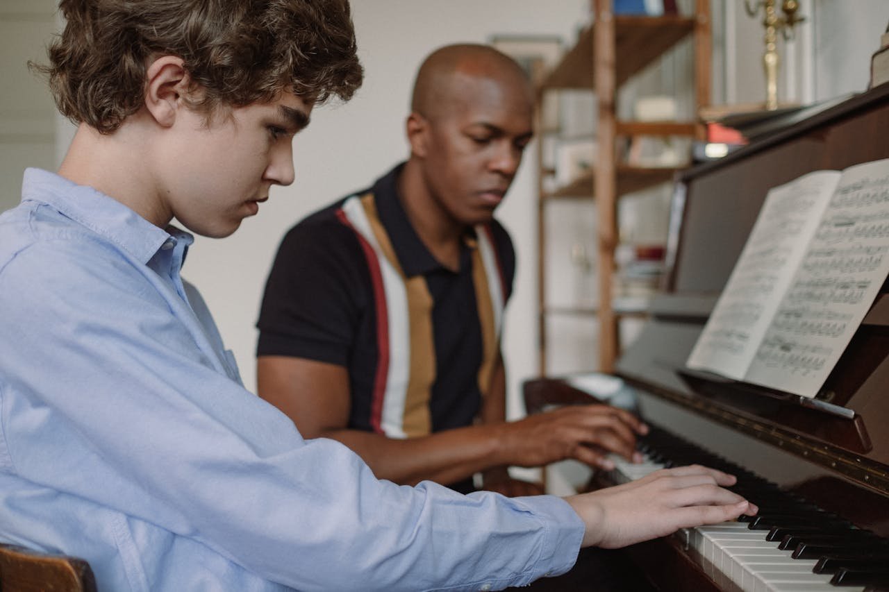 Teen and adult learning piano together in a music lesson indoors, focusing on classical music practice.